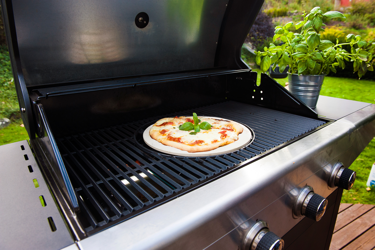 Nygrillet pizza med smeltet ost og frisk basilikum på svart gassgrill i grønn hage.
