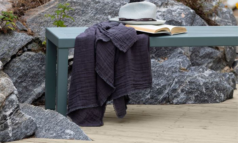 Grønn benk foran grå steiner med mørk lilla duk, åpen bok og hvit hatt