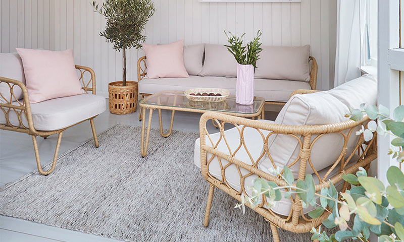 Lyst uterom med rottingmøbler, beige puter, rosa dekorputer og grønne planter.