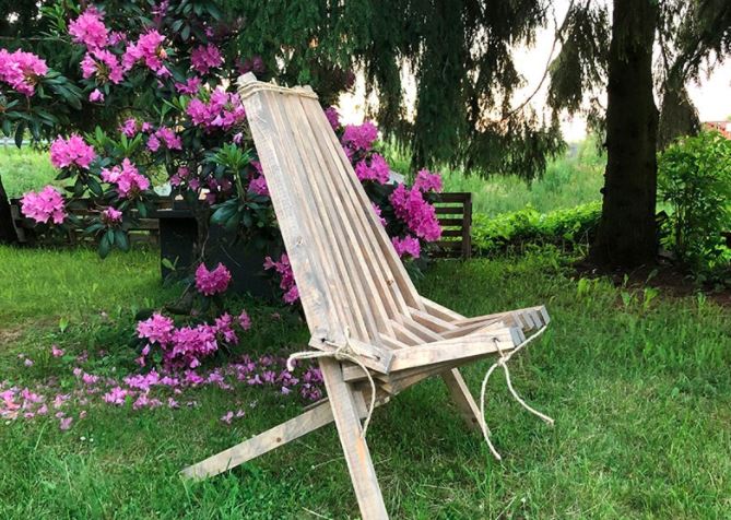 Rustikk tresammenleggbar stol på grønt gress foran rosa rhododendronbusk i hage