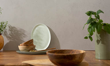 Minimalistisk bordoppsett med hvit oval tallerken, treboller og grønn potteplante.