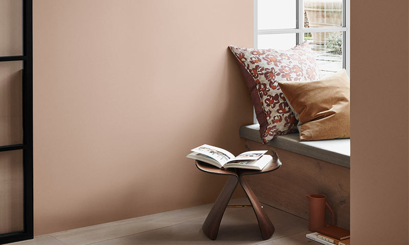 Lite trebord med åpen bok, blomstrete og okergule puter i beige lesekrok ved vindu.