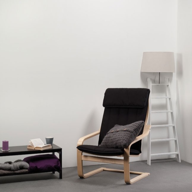 Sort lenestol med lyst tre og grå pute ved hvit stige med lampe og lavt bord med bok og lilla pledd