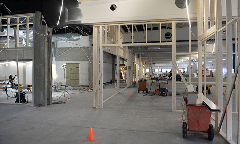 Stor byggeplass med trestendere, betonggulv, røde trillebårer og oransje trafikkjegler