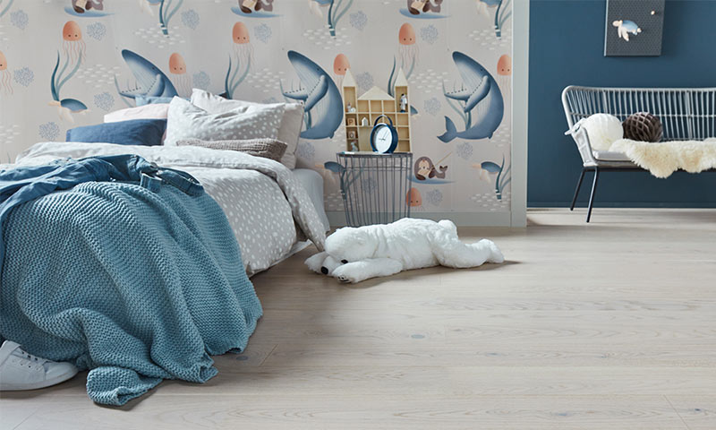 Barnerom med blå-beige vegg med haier og maneter, blått pledd på seng og hvit bamse på lyst gulv.