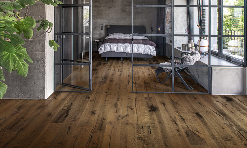 Soverom i industriell stil med mørkt tregulv, glassvegger, seng og lenestol.