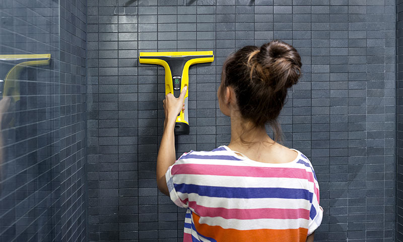Kvinne bakfra i stripet t-skjorte bruker gul nal på mørk flisvegg i dusjen