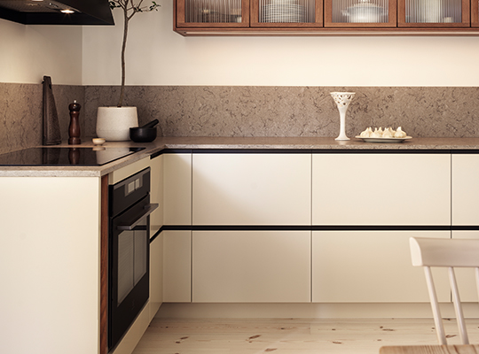 Moderne lyst kjøkkenhjørne med kremhvite skap, grå benkeplate, innebygd ovn og tre-detaljer.