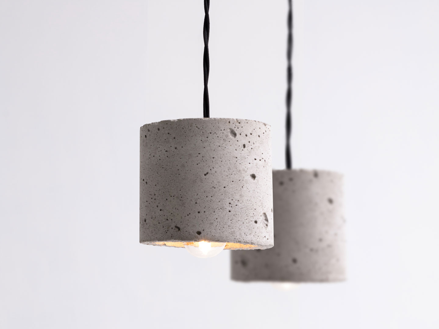 Hengende grå betongpendler i sylinderform med varme lyspærer på hvit bakgrunn