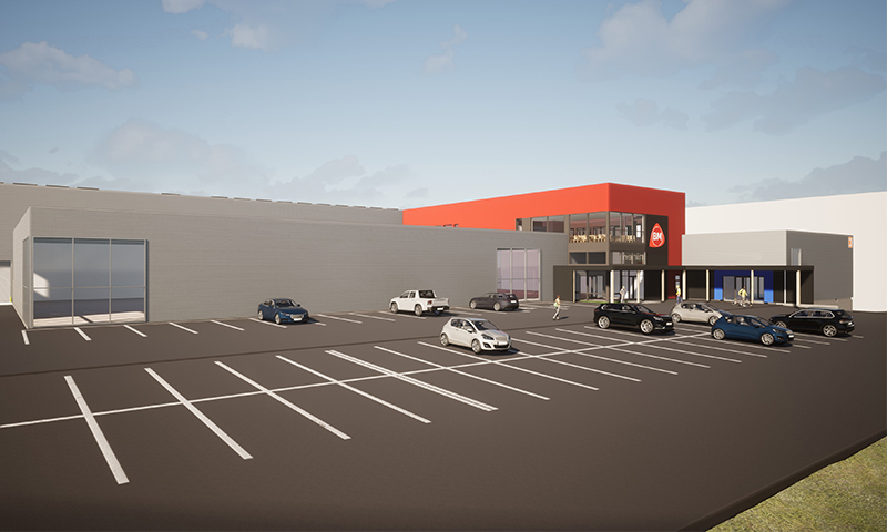Stor grå butikkbygning med rødt inngangsparti og BM-logo, bilparkering foran under blå himmel.