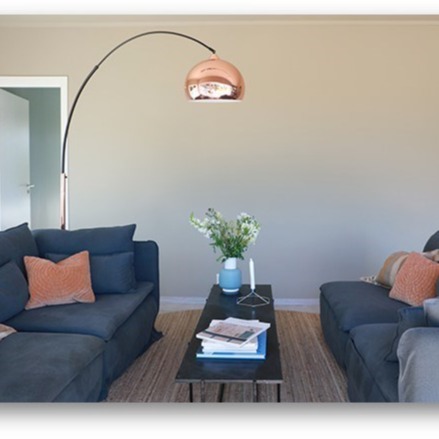 Stue med to grå sofaer med oransje puter, svart salongbord med blomster under kobberlampe.