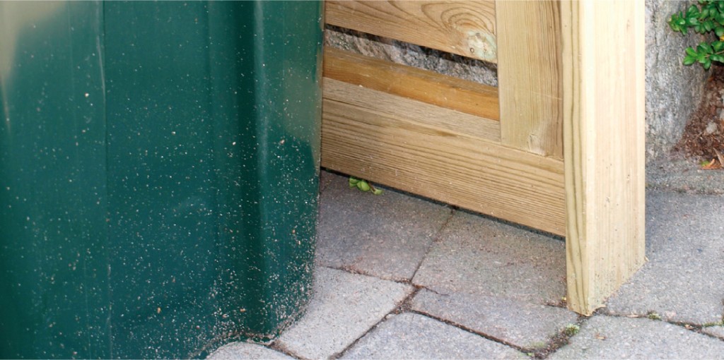 Grønn plastbeholder ved lys treport på grå brostein.