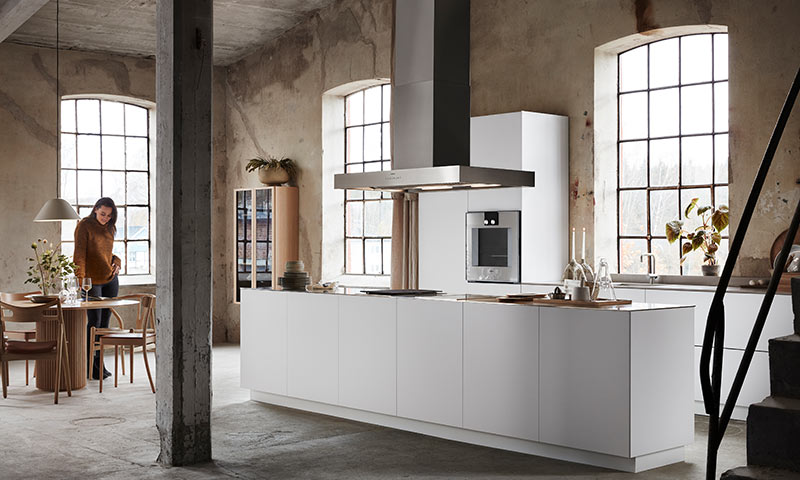 Lyst loftkjøkken i industristil med hvit øy, rå betongvegger og store vinduer.