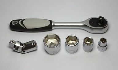 Krommetall skralle med svart-grått grep, fem pipenøkler og leddadapter på grå bakgrunn.