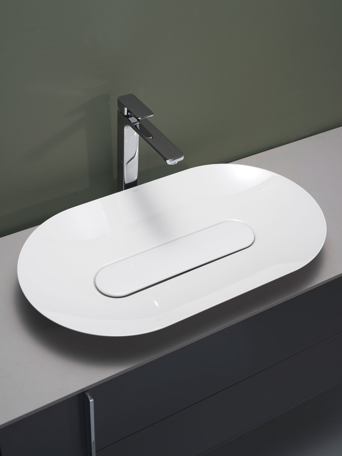 Hvit oval vask med skjult rist på grå benkeplate, høy kromarmatur mot olivengrønn vegg.
