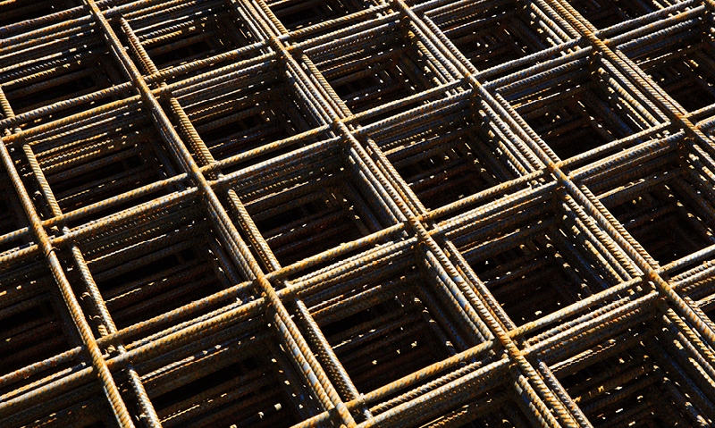 Rustent armeringsnett i stål, sollysspill over firkantet rutenett på byggeplass