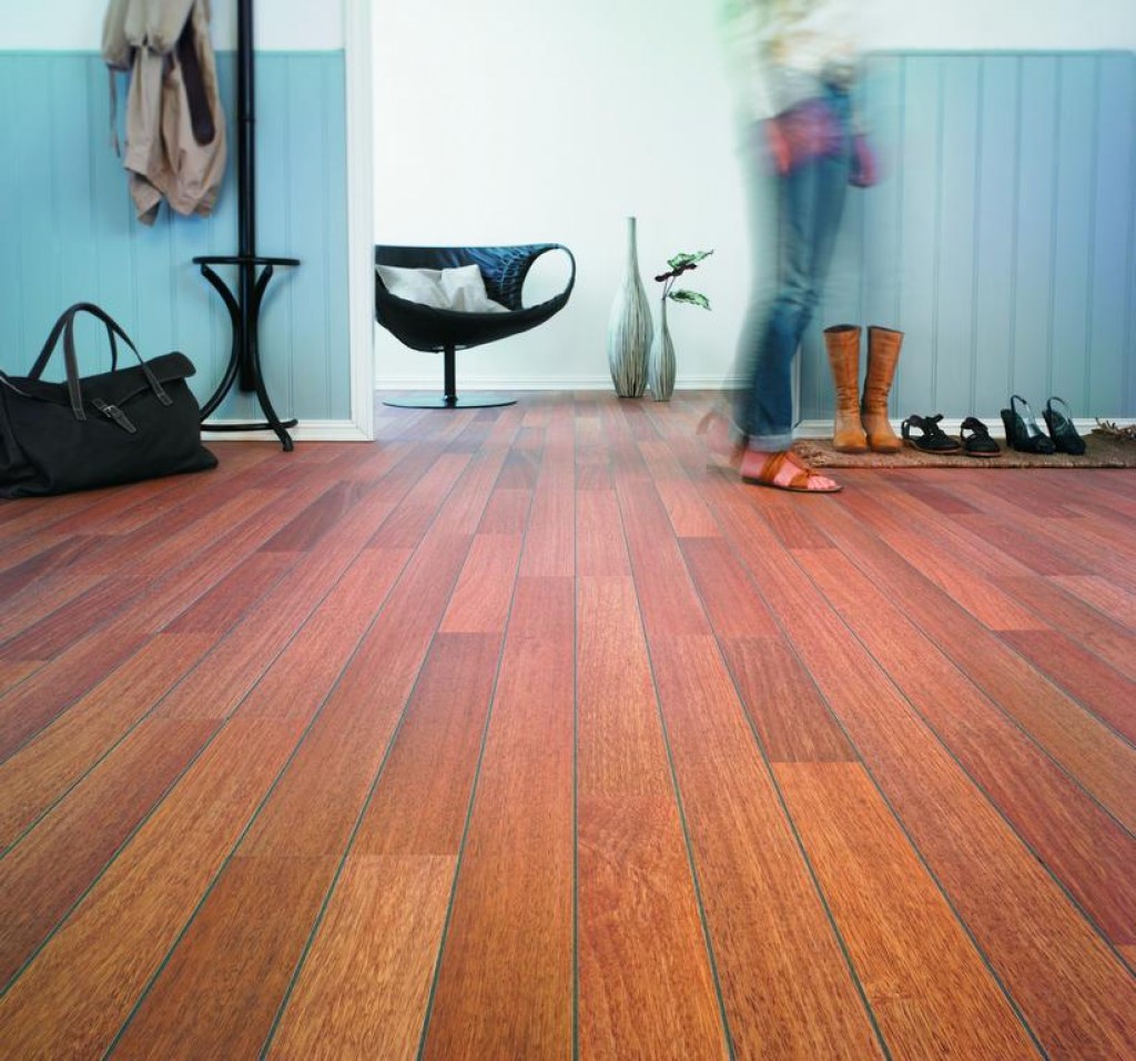 Rødt tregulv i lysblå entré med sko, støvler, svarte møbler og uskarp gående person