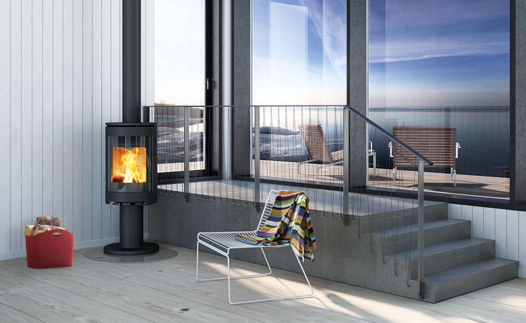 Moderne rom med svart vedovn, flammer, rød vedkurv, stol med farget pledd og havutsikt