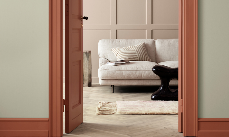 Åpen terrakottadør til stue med lys grå sofa, stripete pute og svart skulpturbord