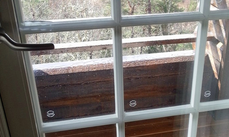 Regnvåte dråper på hvit vindusrute med utsikt mot mørk trekledning på balkong