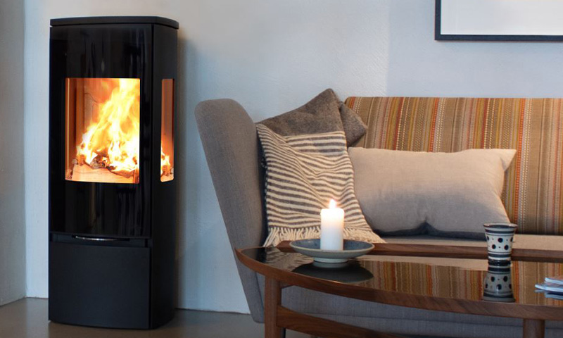 Koselig stue med svart vedovn og flamme, stripet beige sofa, grå lenestol og tent stearinlys