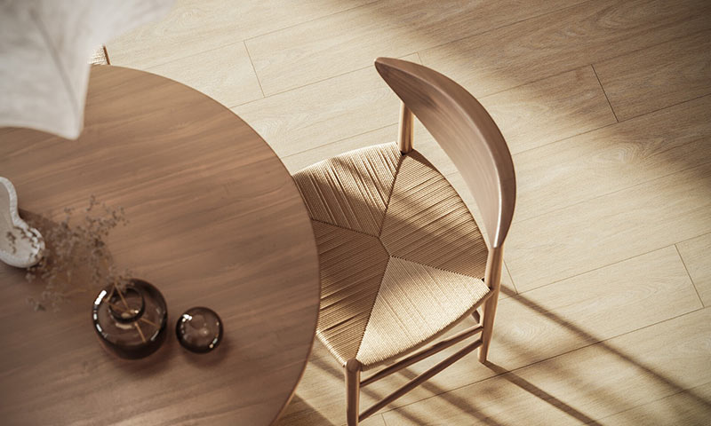 Fugleperspektiv av rundt brun bord med glassvase, beige flettet stol og sollys på lyst tregulv