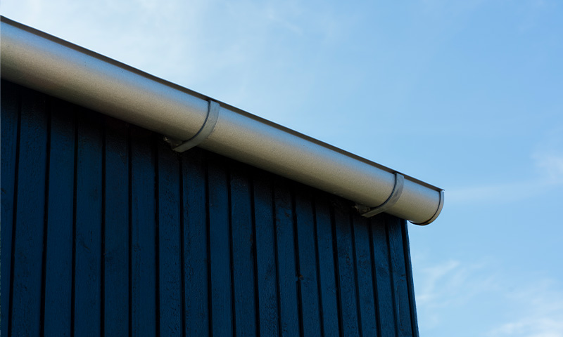 Blå, vertikal tremurvegg med sølvgrå takrenne mot lys blå himmel