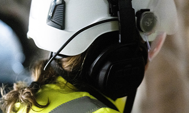 Bakside av arbeider med hvit hjelm, øreklokker og gul refleksvest.