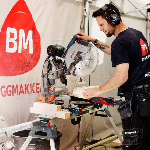 Mann med hørselvern sager treplanker på Bosch gjærsag foran rød BM-logo i lyst telt