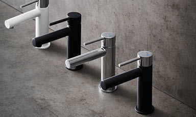 Fire moderne sylinderblandebatterier i hvitt, sort og krom på grå betongoverflate.