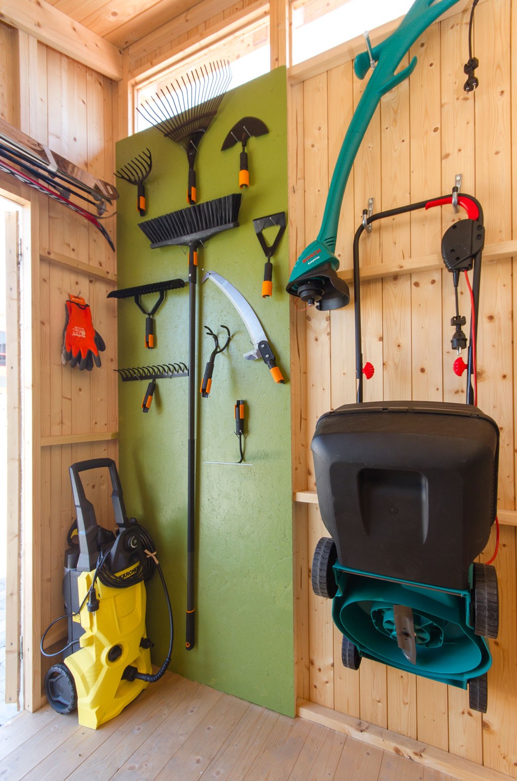 Lyst tre-skur med grønn tavle av oransje-håndtakede hageredskaper gul høytrykkspyler og grønn trimmer