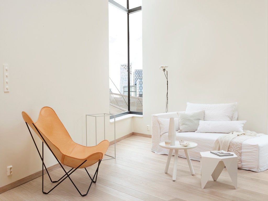 Lyst, minimalistisk rom med beige skinnfåtølje, hvit sofa, små bord og hjørnevindu