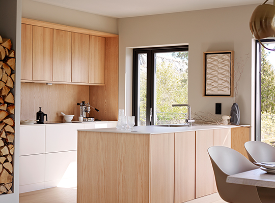 Moderne kjøkkenøy i lyst tre med hvite stoler og vindu mot grønt uteområde.