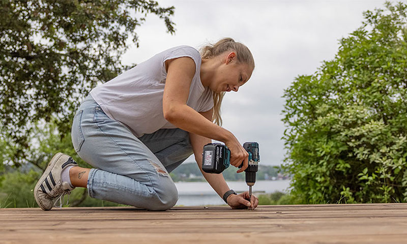 kvinne bruker elverktøy for å skru i terrassebord