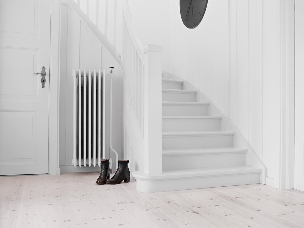 Hvitt inngangsparti med lyst eikegulv, svevende trapper, radiator, svarte ankelstøvler