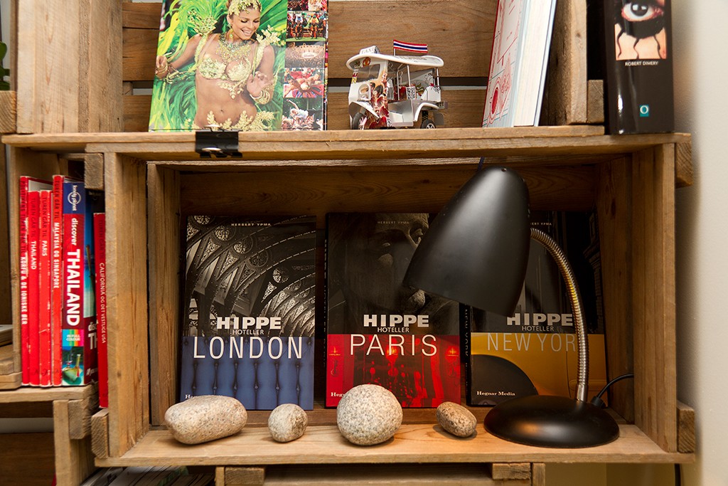 Hylle med fargesterke London-, Paris- og New York-guider, svart lampe, små steiner og mini tuk-tuk.