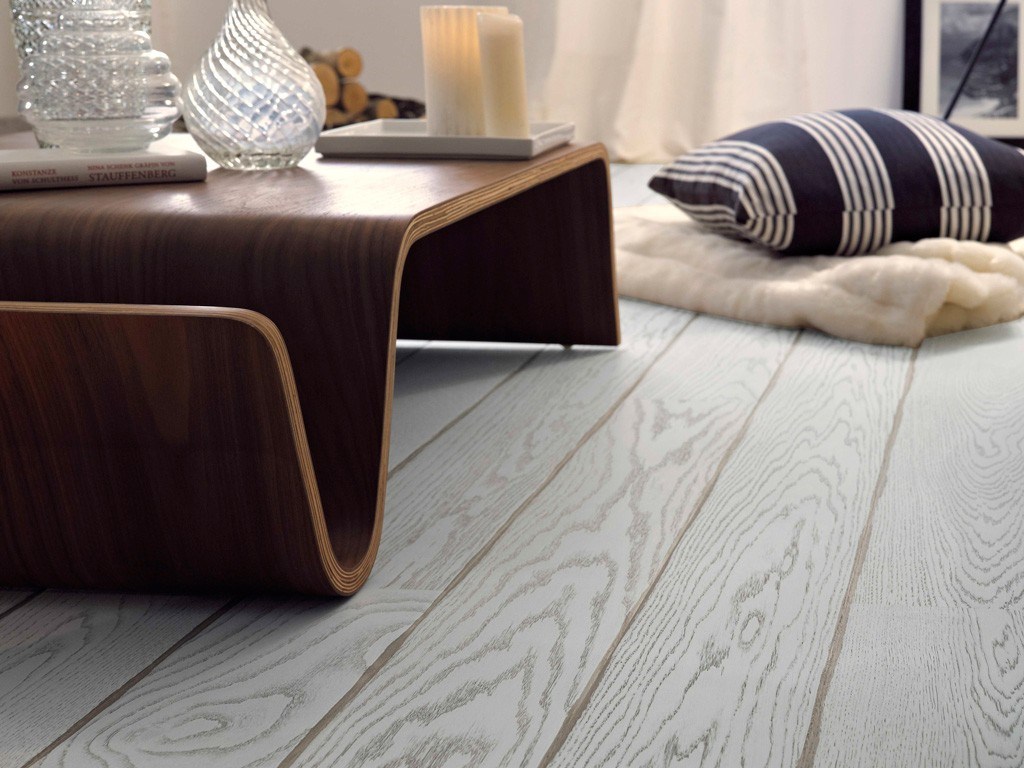 Bølgende mørkt trebord på lyst grått tregulv, glassvaser, lys og stripete pute på ullteppe.