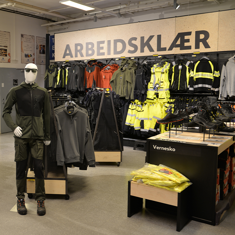 Butikkinteriør med arbeidsklær: dukke kledd i grønt, oransje og neongule jakker, vernesko