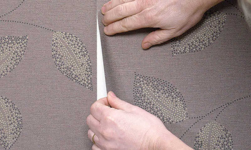 To hender justerer søm på brunt tapet med grafiske blader i beige og mørkebrunt.