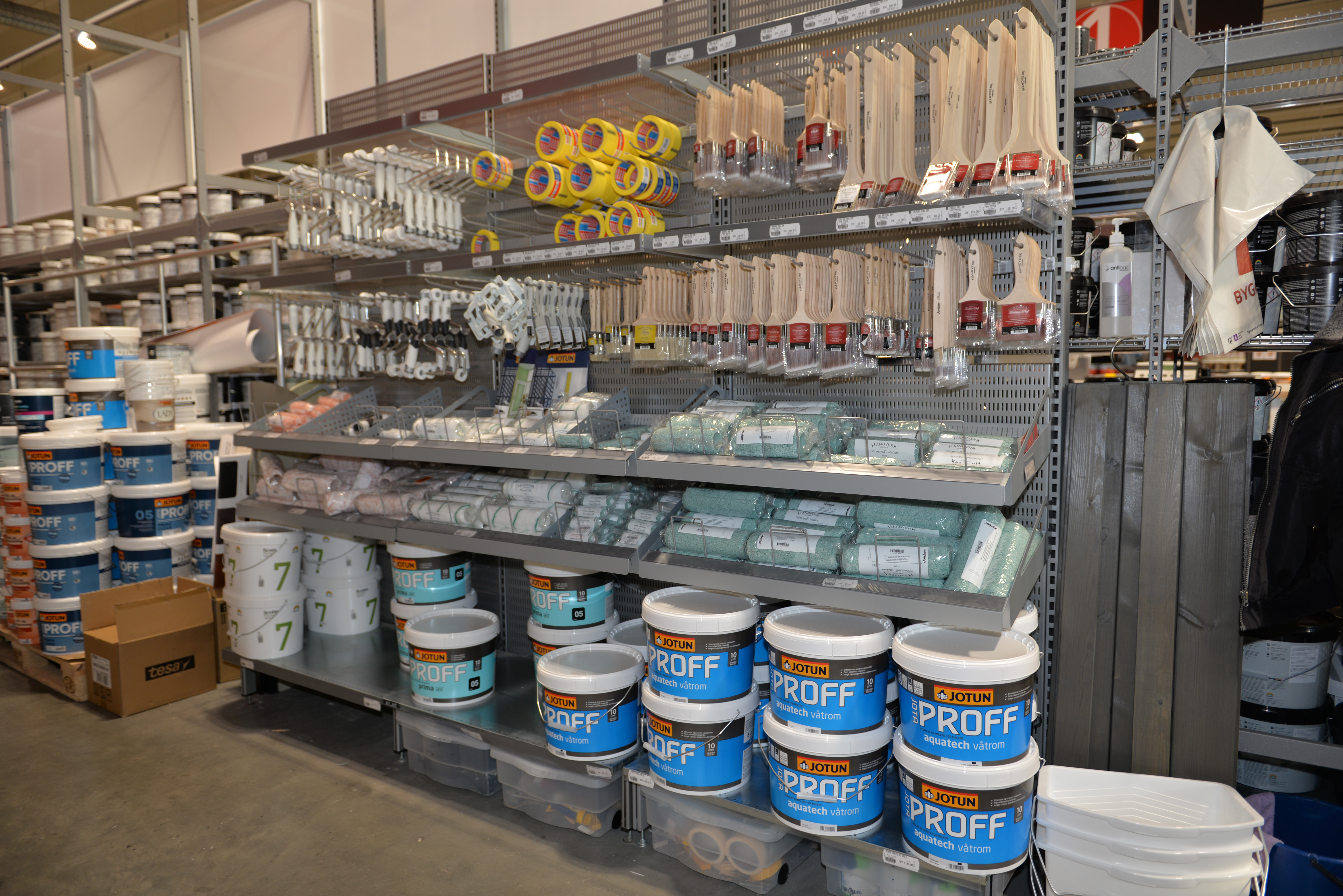 Butikkhylle med blå malingsspann, pensler, maleruller og gult maskeringstape.