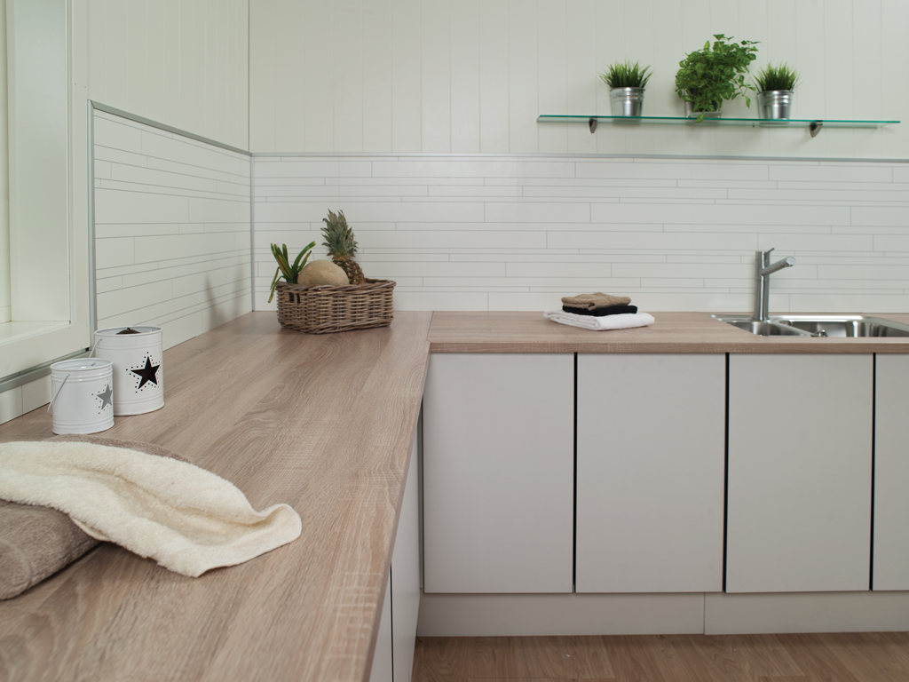 Moderne kjøkkenbenk med treplate, lysegrå skap, kurv med ananas og frukt, håndklær, planter