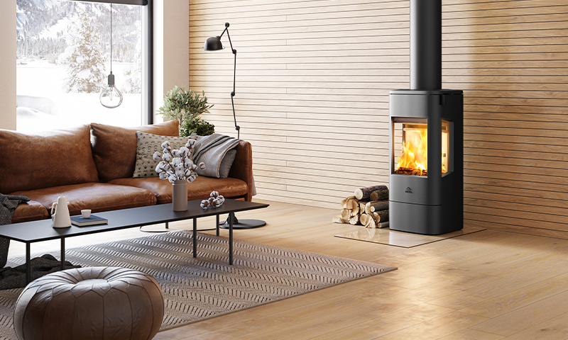 Lys stue med trepanel, brun skinnsofa, svart peisovn med ild, kaffebord og snødekt utsikt