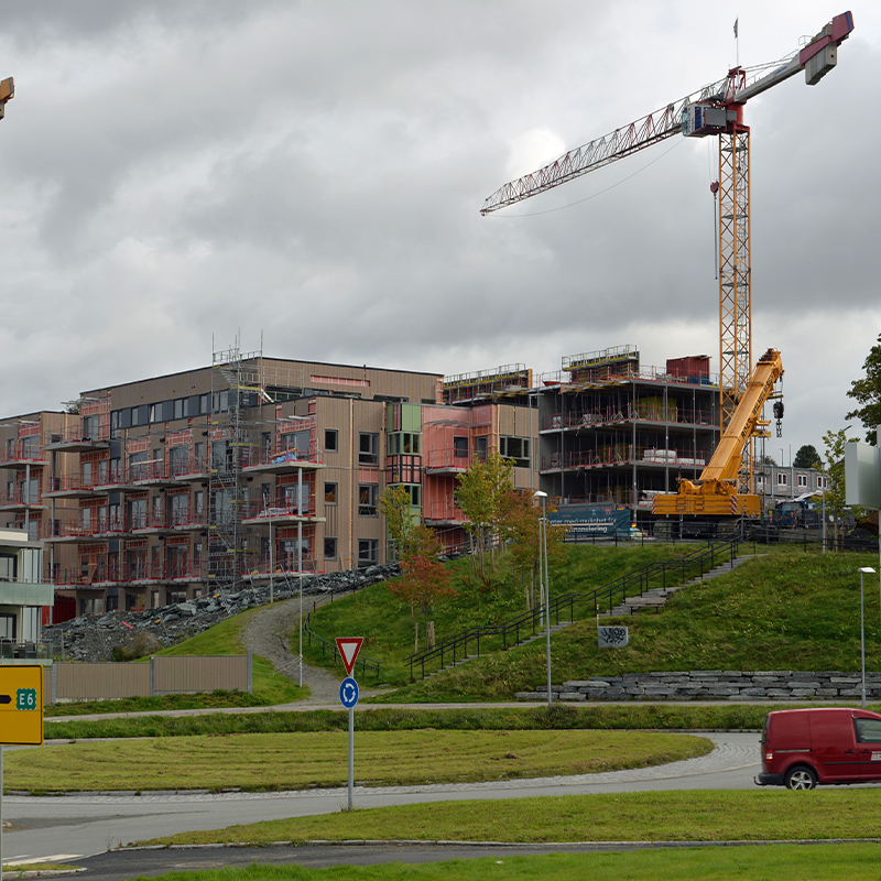 Stor byggeplass med fleretasjers trebygninger, gul kran og overskyet himmel