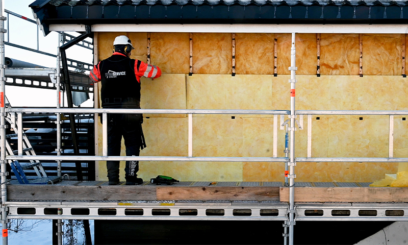 Arbeider på stillas monterer gule isolasjonspaneler på husfasade under svart tak