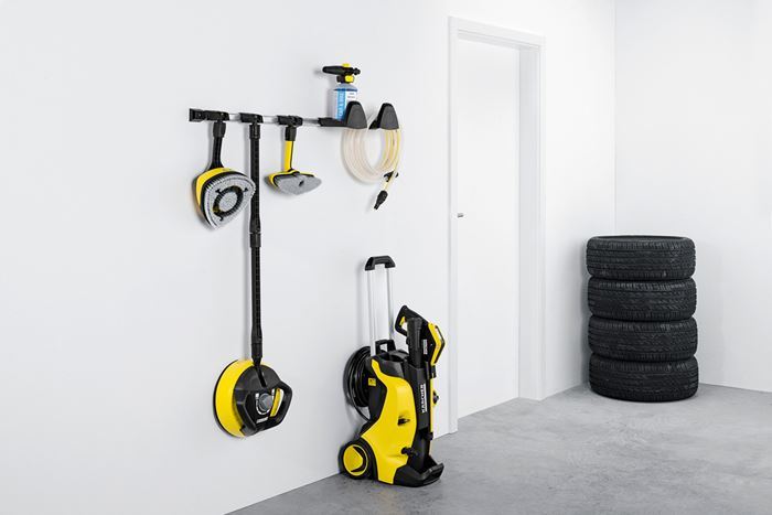 Gul-svart høytrykkspyler med tilbehør hengt på hvit vegg ved stabel av svarte bildekk.