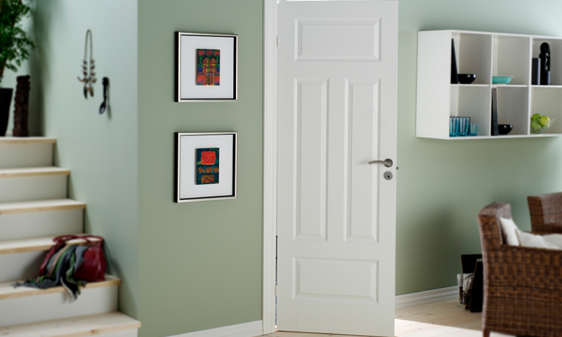 Hjemmeinteriør med grønn vegg, åpen hvit dør, to innrammede fargerike bilder, hylle med glass