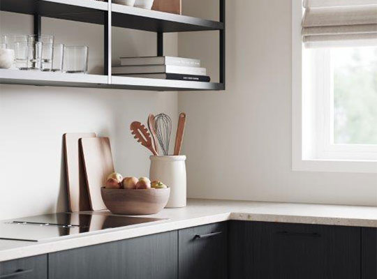 Moderne kjøkkenhjørne med svarte skap, hvit benkeplate, åpne hyller, eplebolle og redskaper