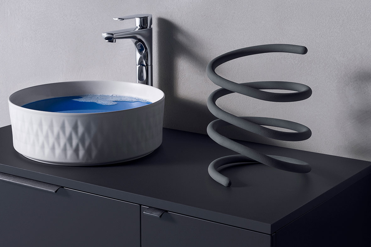 Mørk grå baderomsbenk med hvit rund servant fylt med blått vann, krom kran og grå spiral.