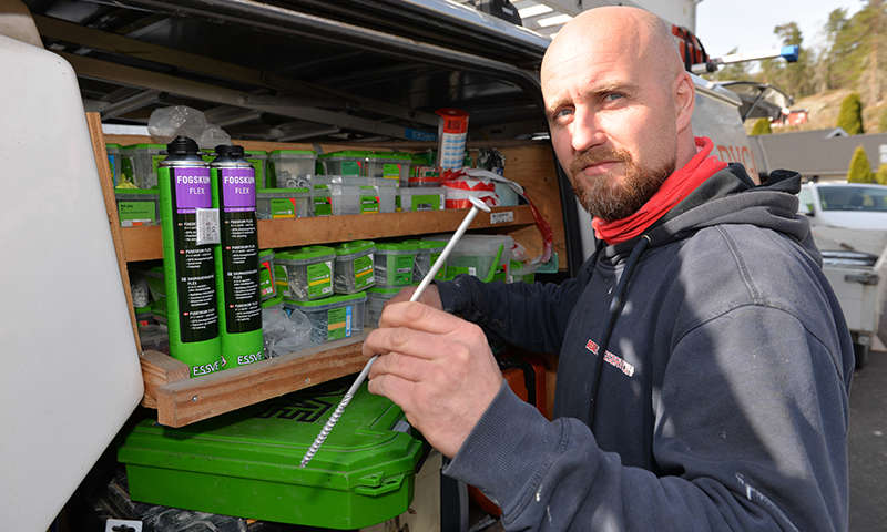 Håndverker trekker dyse fra hylle med grønne fugepatroner i varebil