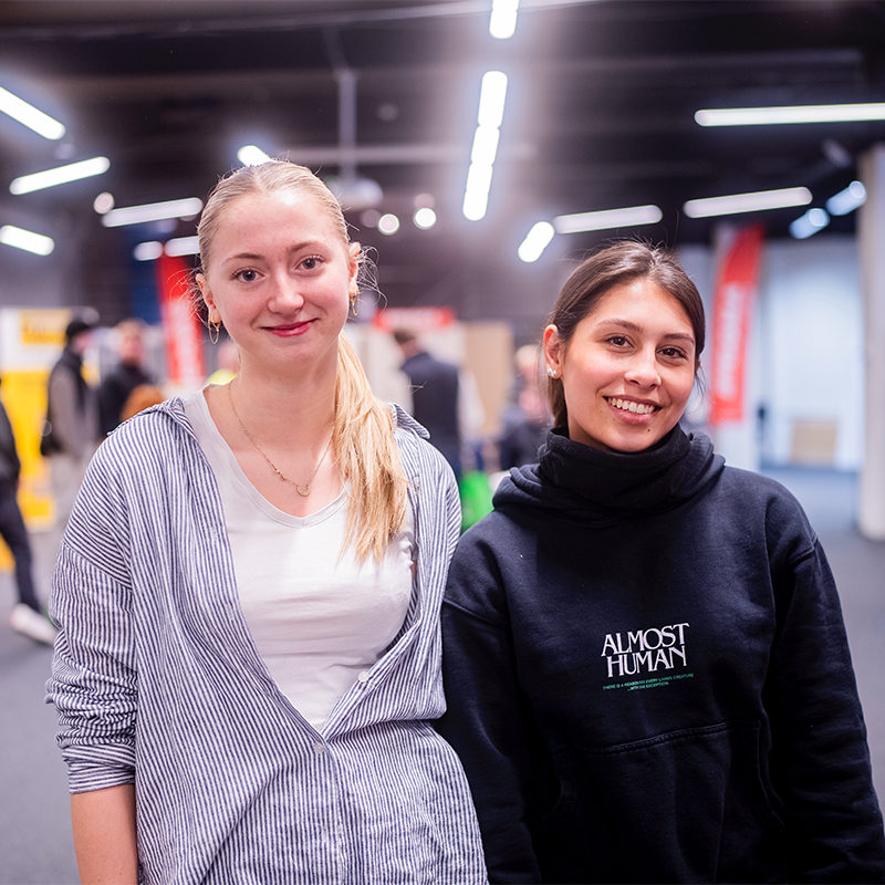 To kvinner i messehall, én i blåstripet skjorte og én i svart Almost Human-genser